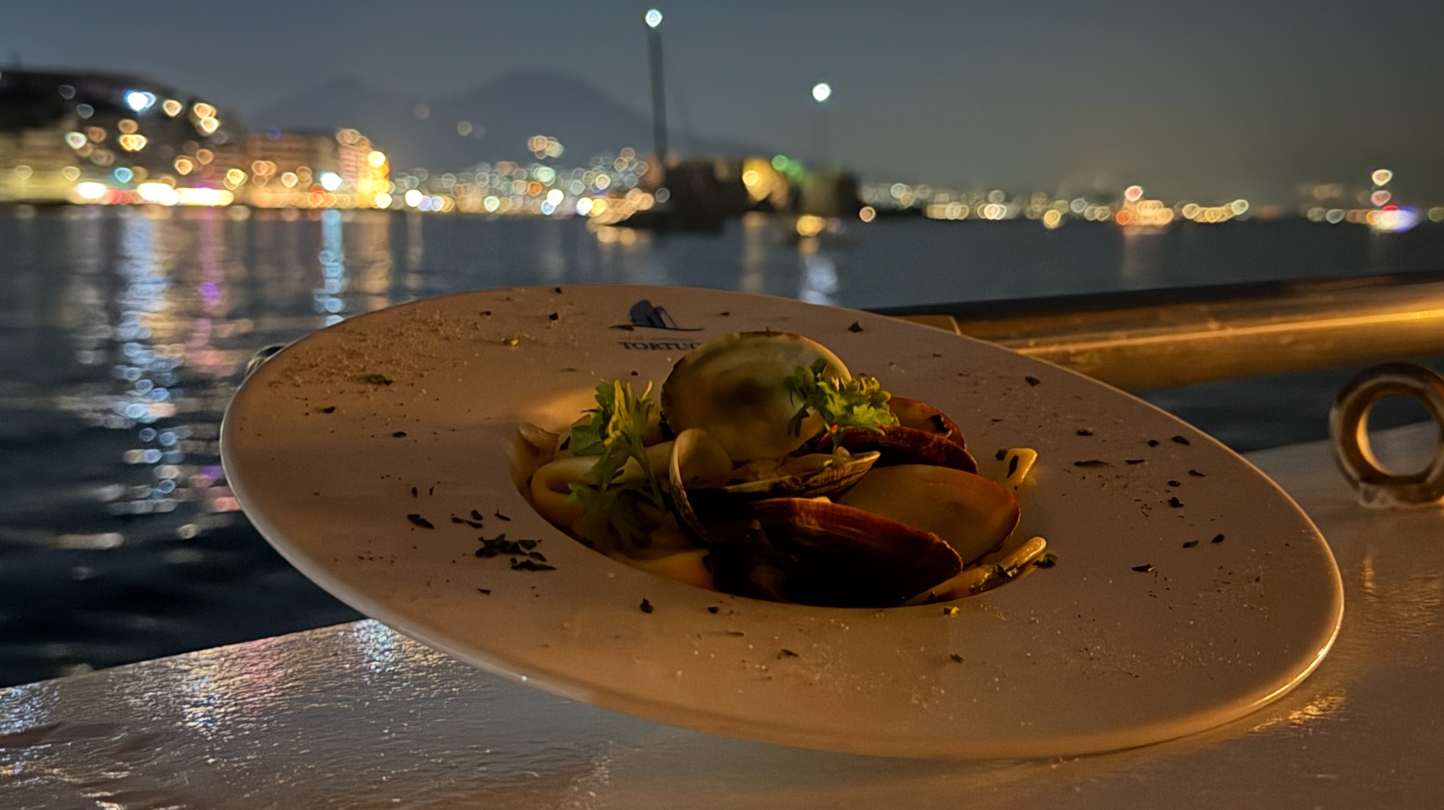 Scialatielli alle vongole serviti a bordo del Veliero Tortuga con Napoli illuminata sullo sfondo