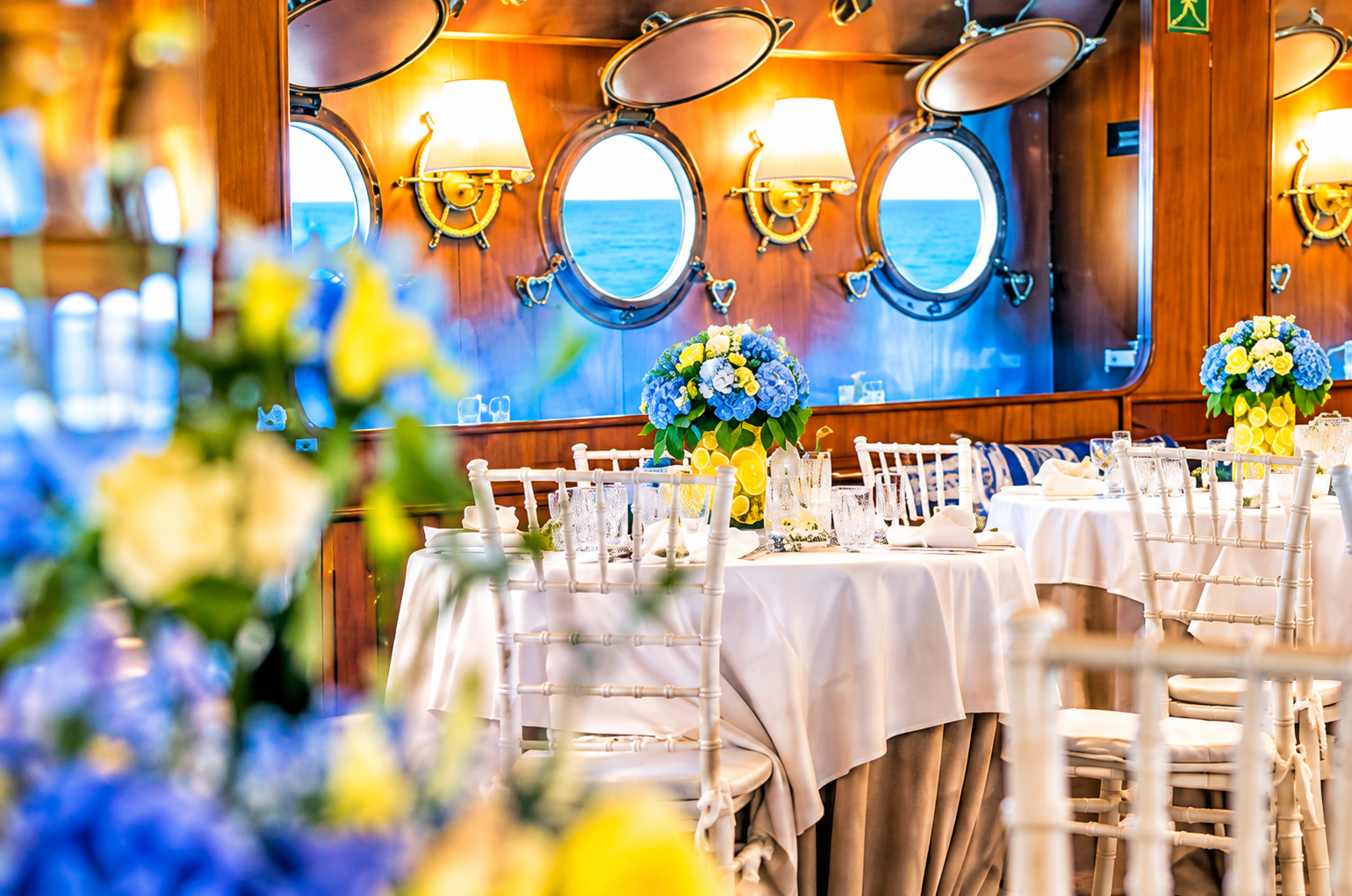 Sala ristorante del Veliero Tortuga allestita con fiori azzurri e gialli, tavoli eleganti e vista sul mare